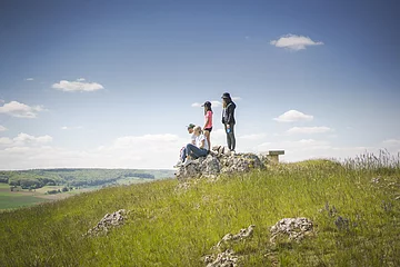 Familie mit Hund sitzen auf dem Bubenheimer Berg auf einem Felsen. Kinder stehen hinter den Eltern